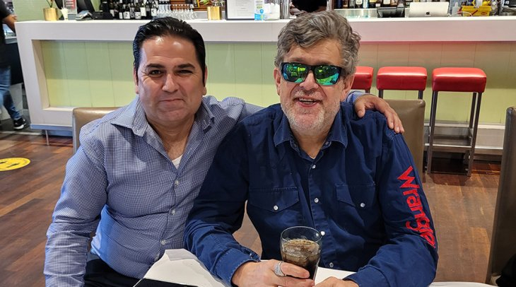 A middle aged male NDIS participant sitting with a soft drink, sitting next to his Enhanced Lifestyles Disability Support Worker.