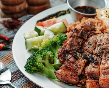 Sliced steak and egg, sitting on a flavoured rice, with broccoli, tomato and cucumber with a spicy chilli dip