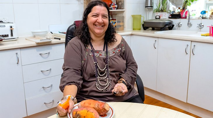 Female NDIS participant sitting in her kitchen peeling sweet potato