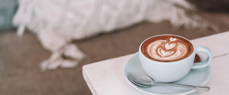Coffee cup with a spoon sitting and biscotti sitting on the saucer on a white table