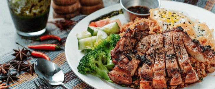 Sliced steak and egg, sitting on a flavoured rice, with broccoli, tomato and cucumber with a spicy chilli dip