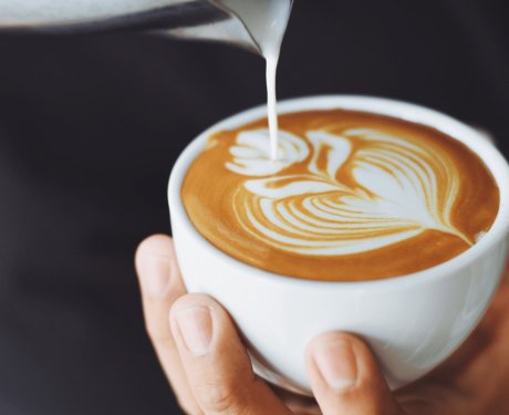 A man holding a coffee cup in his hand, creating milk art